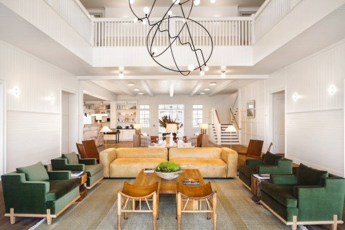 Bright, modern living room with a large sofa, green chairs, a wooden table, and a unique chandelier. Open layout with natural light.