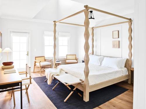Bright, modern bedroom featuring a four-poster bed, wooden furniture, and large windows for natural light.