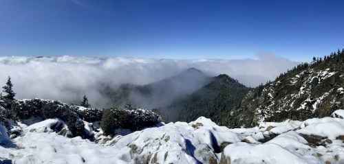 A panoramic view of snow-covered mountains and clouds under a clear blue sky.