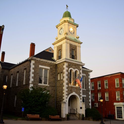 Historic building with a clock tower, American flag, and surrounding greenery, illuminated by evening light.