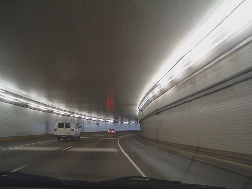 A view from inside a tunnel, with vehicles driving on a curved road and illuminated walls.