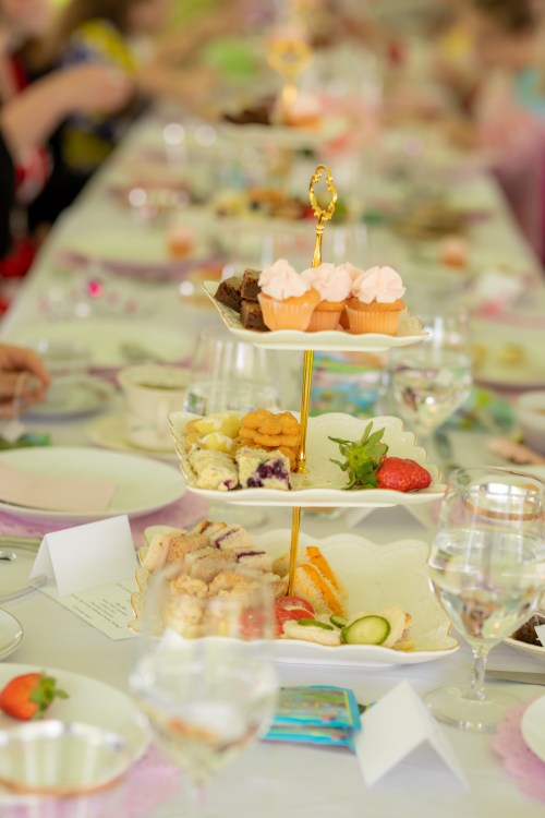 A tiered dessert stand with cupcakes and treats, surrounded by elegantly set tables and guests enjoying a gathering.