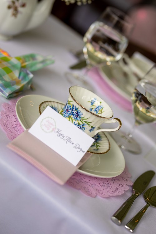 A beautifully set table with a floral teacup, place card, and elegant glassware on a white tablecloth.