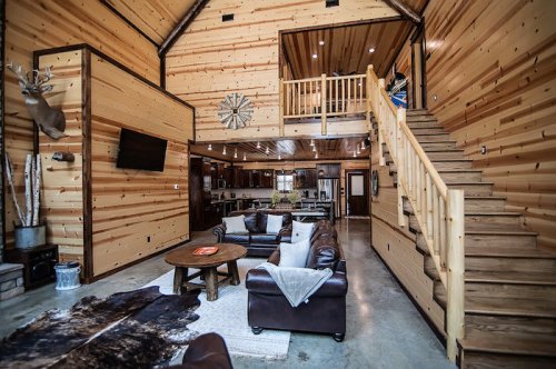 Cozy wooden interior of a cabin with a living area, staircase, and open kitchen, featuring rustic decor and natural light.