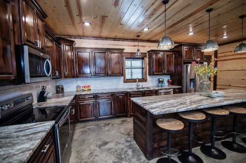 Modern kitchen with dark wooden cabinets, granite countertops, and a large island with bar stools, featuring rustic decor.