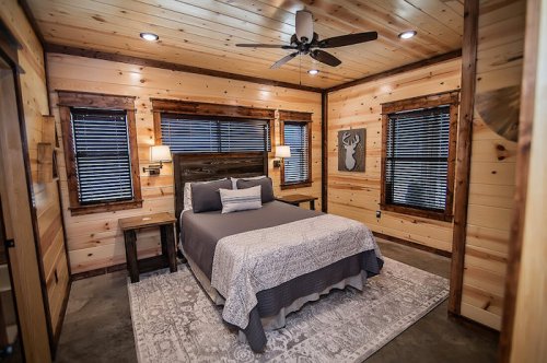 Cozy wooden bedroom with a queen bed, nightstands, and large windows, featuring rustic decor and warm lighting.