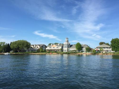 A serene lakeside view featuring a large building with a tower, surrounded by trees and a clear blue sky.