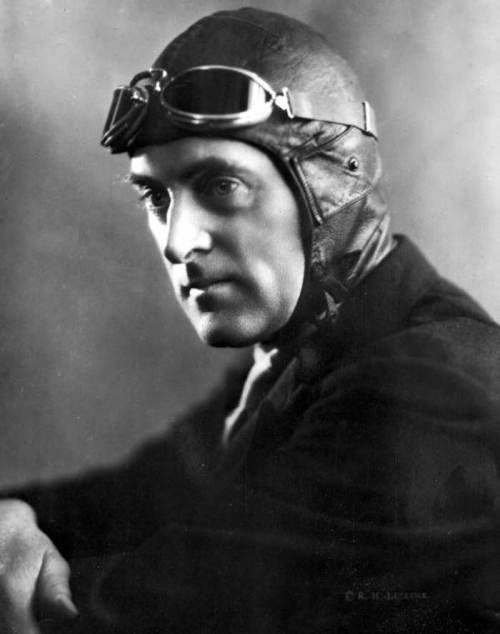 A vintage portrait of a man in a leather aviator cap and goggles, looking thoughtfully to the side.