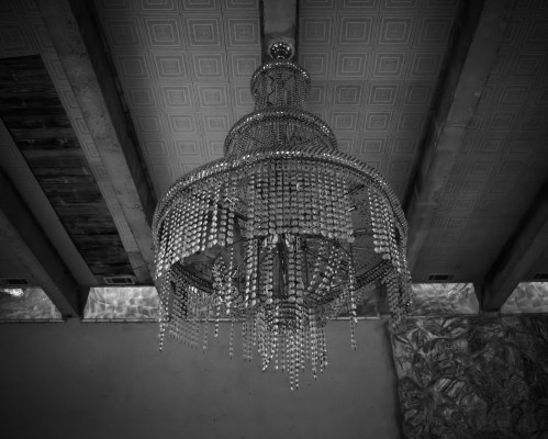 A large, ornate chandelier hangs from a ceiling with wooden beams, captured in black and white.