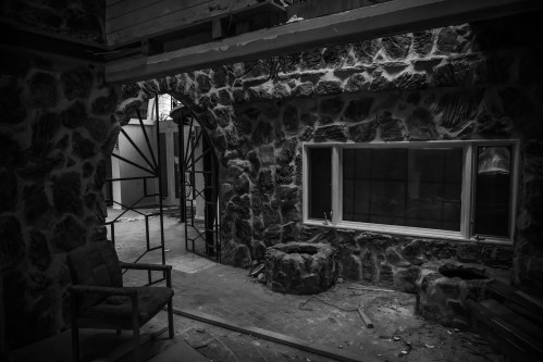 Abandoned interior with stone walls, a broken window, and a chair in a dimly lit space.