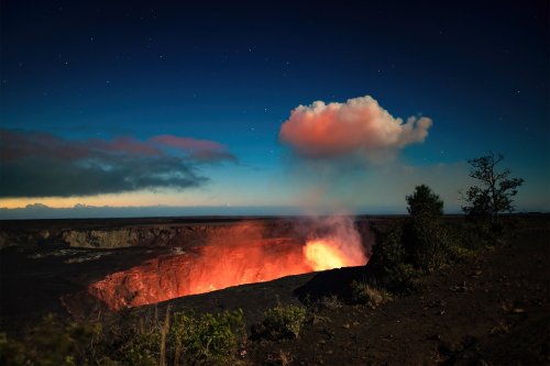 A glowing volcano at night, with smoke rising against a starry sky and a colorful cloud above the crater.