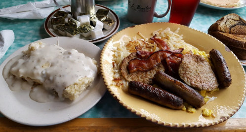 A hearty breakfast plate with eggs, bacon, sausage, hash browns, and a side of biscuits smothered in gravy.