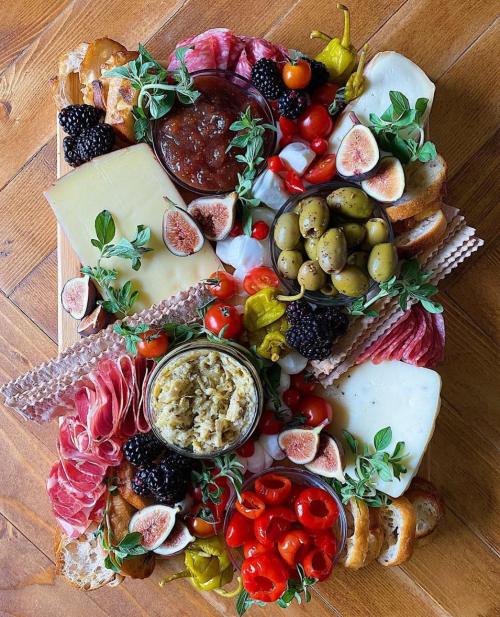 A colorful charcuterie board featuring meats, cheeses, olives, figs, tomatoes, and herbs on a wooden surface.