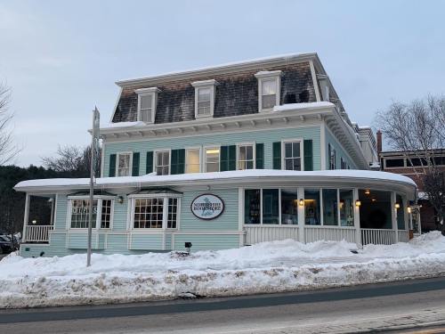 A charming blue building with white trim, surrounded by snow, featuring a sign for "Northeast Bed & Breakfast."