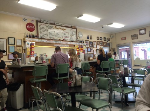 A retro diner interior with green chairs, a counter, and patrons enjoying their meals amidst vintage decor.