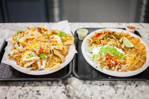 Two trays of Mexican food: one with loaded nachos and the other with grilled chicken, rice, and vegetables.