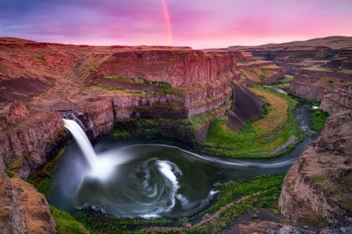 A stunning waterfall cascades into a winding river, surrounded by rocky cliffs and vibrant greenery under a colorful sky.