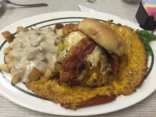 A large burger topped with bacon and cheese, served with a side of creamy potatoes and gravy on a white plate.