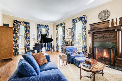 A cozy living room featuring a grand piano, blue floral curtains, a fireplace, and comfortable seating.