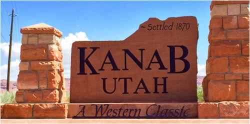 Sign welcoming visitors to Kanab, Utah, established in 1870, with a backdrop of blue skies and red rock formations.