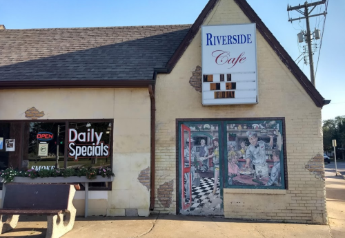 Exterior of Riverside Cafe featuring a mural, open sign, and a daily specials board.