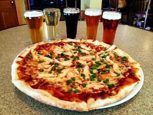 A pizza topped with chicken and green onions, accompanied by five glasses of different beers on a table.