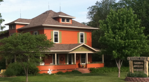 A vibrant orange two-story house with a porch, surrounded by greenery and a sign for "Windom Inn."