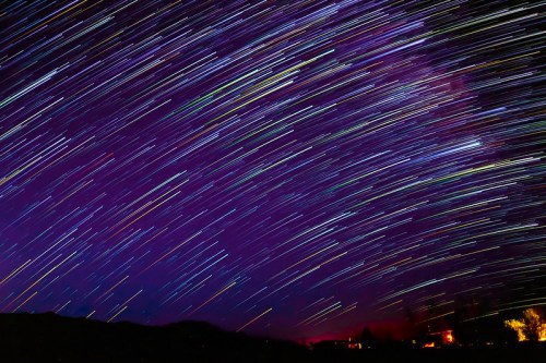 A vibrant night sky with streaks of stars creating a colorful, swirling effect over a dark landscape.