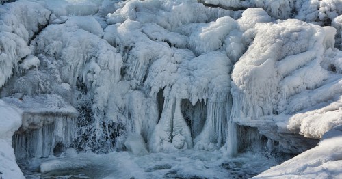 Frozen waterfall with icicles and ice formations, cascading water partially visible beneath the ice.
