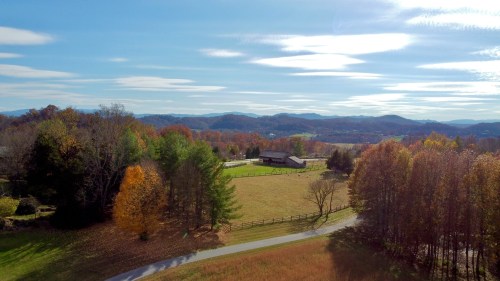 A scenic view of rolling hills and colorful autumn trees under a clear blue sky. A barn is visible in the distance.