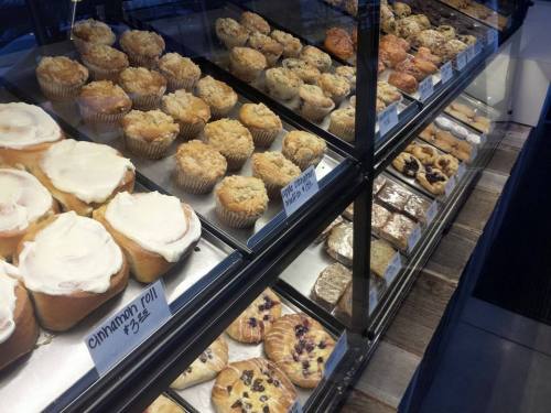A display case filled with various baked goods, including muffins, cinnamon rolls, and pastries.