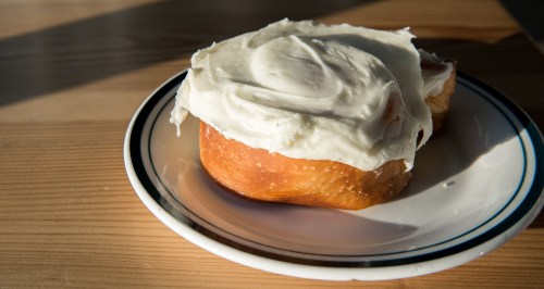 A cinnamon roll with thick white frosting on a plate, sitting on a wooden table.