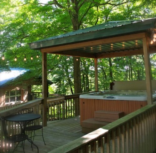 A wooden deck with a hot tub, surrounded by trees and string lights, creating a cozy outdoor space.