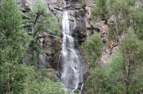 A cascading waterfall flows down rocky cliffs, surrounded by lush green trees and foliage.