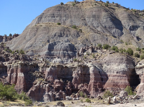 A rugged mountain landscape featuring layered rock formations and sparse vegetation under a clear blue sky.
