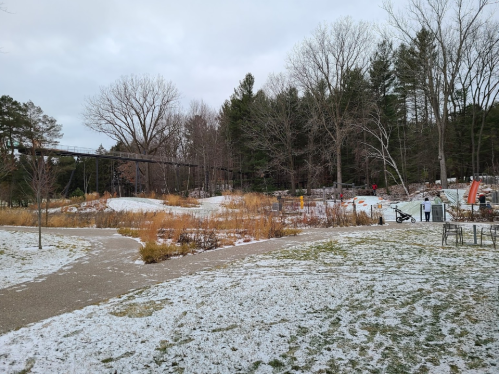 A snowy park scene with bare trees, a winding path, and playground equipment in the background.