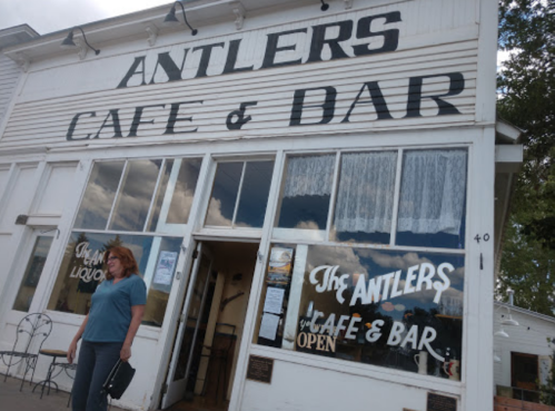 A woman stands outside the Antlers Cafe & Bar, featuring large signage and a welcoming entrance.