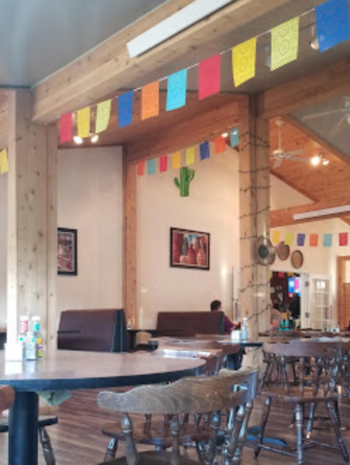 A cozy restaurant interior with wooden beams, colorful banners, and a cactus decoration on the wall.