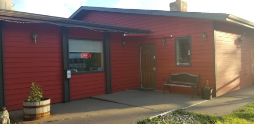 A red building with an "OPEN" sign, featuring a wooden door and a bench outside.