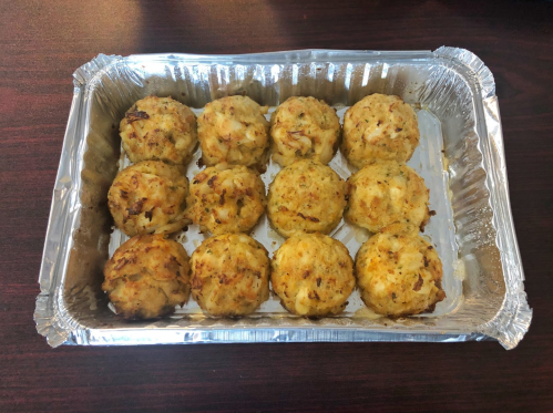A tray of twelve golden-brown crab cakes arranged neatly in a silver aluminum pan.