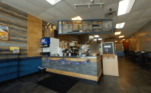 Interior of a casual eatery featuring a counter, menu board, and seating area with wooden accents and festive decor.