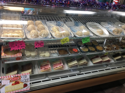 Display case filled with various desserts, including cookies, cakes, and pastries, with colorful price tags.
