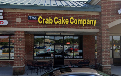 Exterior of The Crab Cake Company restaurant, featuring a brick facade, large windows, and outdoor seating.
