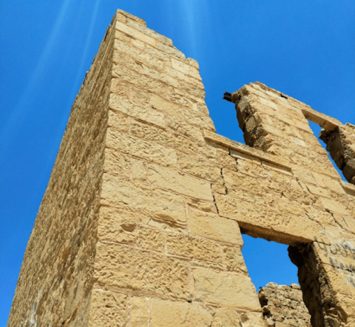 Ruins of a stone structure against a clear blue sky, showcasing weathered walls and an open window.
