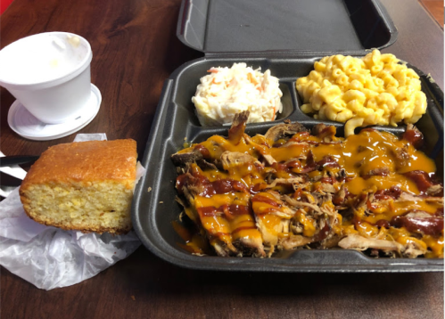 A takeout tray with pulled pork topped with barbecue sauce, macaroni and cheese, coleslaw, and a piece of cornbread.