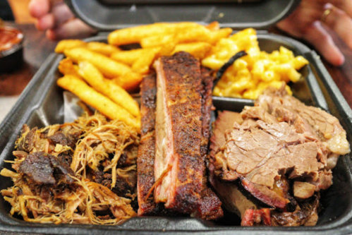 A takeout container filled with pulled pork, brisket, ribs, fries, and macaroni and cheese.