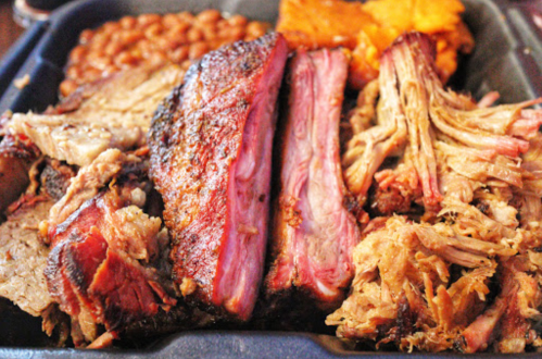 A close-up of a barbecue platter featuring smoked meats, baked beans, and sweet potato.