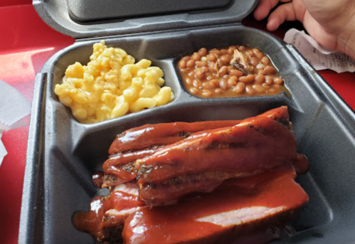 A takeout container with barbecue ribs, macaroni and cheese, and baked beans.