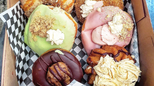 A box of assorted colorful donuts topped with frosting, whipped cream, and various sprinkles and crumbs.