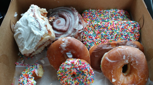 A box of assorted pastries, including cinnamon rolls and colorful sprinkled donuts.